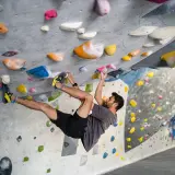 Hombre escalando en un rocódromo interior, superando diferentes grados escalada boulder con agarres de colores.