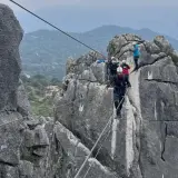 Grupo de personas superando diferentes niveles de vía ferrata, asegurados a cables de acero sobre rocas escarpadas.