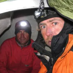 Oscar Pérez, alpinista, y su compañero en una tienda de campaña, ambos con linternas frontales encendidas.