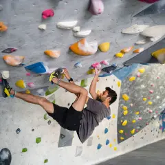 Hombre escalando en un rocódromo interior, superando diferentes grados escalada boulder con agarres de colores.