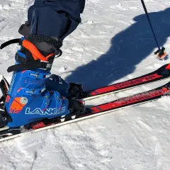 Esquiador listo para la acción con sus botas de esquí termoformables Lange azules y naranjas, fijadas a esquís Dynastar rojos.
