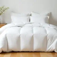 Cama blanca con un edredón mullido, almohadas y un jarrón con flores. El plumón es tan suave que querrás acurrucarte.