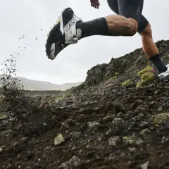 Corredor en terreno rocoso, levantando tierra con su zapatilla Hoka equipada con suela Vibram Megagrip.