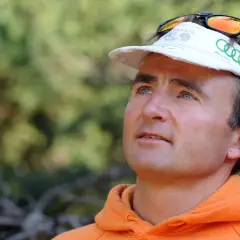 Ueli Steck, con gorra blanca y sudadera naranja, mira hacia arriba con determinación.