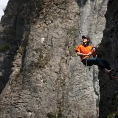 Dean Potter desciende por una pared rocosa, con el sol brillando sobre su camiseta naranja.