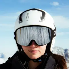 Mujer con casco de esquí blanco y gafas espejadas, lista para deslizarse por la montaña.