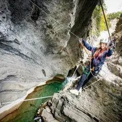 Mujer sonríe mientras cruza un barranco usando técnicas de escalada y tirolina. Otro escalador la sigue.