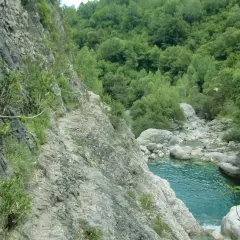 Sendero rocoso con cuerda de seguridad a lo largo de la pared de la garganta de Escuain, con un río turquesa y vegetación exuberante al fondo.