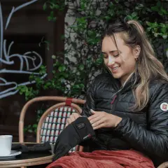 Mujer sonríe mientras se pone guantes térmicos, perfectos para el frío. Una taza de café la espera.