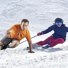 Instructor demuestra ejercicios para esquiar, con un esquiador en la nieve.