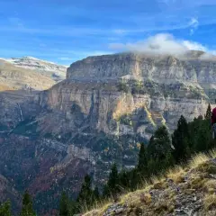 Senderista admira imponentes acantilados y cascadas en las rutas Pirineos. El otoño tiñe el valle de colores cálidos.