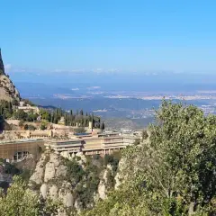 Vista panorámica del monasterio de Sant Miquel de Montserrat, con sus edificios anclados a la montaña y el valle extendiéndose hasta el horizonte.