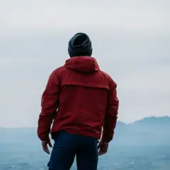 Hombre con chaqueta roja y gorro azul, contemplando el paisaje. ¿Primoloft vs Gore-Tex para esta aventura?