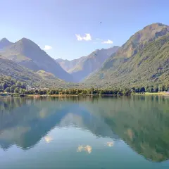 Tranquilo lac de Genos con montañas verdes y paracaidistas en el cielo azul.