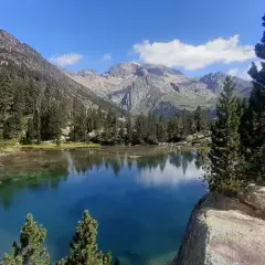 El ibonet de Batisielles, un espejo de agua turquesa rodeado de pinos y montañas imponentes, refleja el cielo azul y las nubes.
