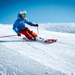Esquiador con chaqueta azul y pantalones naranjas desciende una pista nevada, demostrando como se esquia con agilidad y estilo.