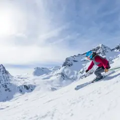 Esquiadora desciende por una ladera nevada en el Pirineo Aragonés, con picos majestuosos de fondo.