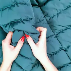 Manos con uñas rojas arrugan una chaqueta verde oscuro recién lavada.