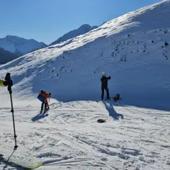 Un grupo de esquiadores se prepara para el esqui extremo en una ladera nevada, con picos montañosos al fondo.