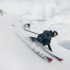 Dos esquiadores disfrutan de un descenso vertiginoso en esqui alpino, levantando nieve en su camino.