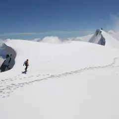 Dani Arnold camina por una cresta nevada, dejando huellas en el camino hacia la cima.