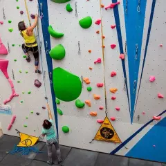 Dos escaladoras practican en un rocódromo, un muro artificial con presas de colores para trepar.