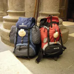 Dos mochilas, una azul y otra roja, con conchas de peregrino, listas para el camino. El tamaño de la mochila es clave para el Camino de Santiago.