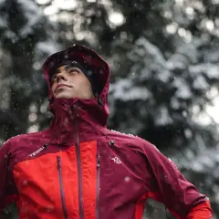 Hombre con ropa para ir a la montaña, con capucha y chaqueta impermeable, bajo una nevada.