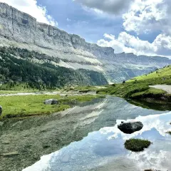 Un lago sereno refleja las imponentes montañas y el cielo nublado en el Parque Nacional de los Pirineos.