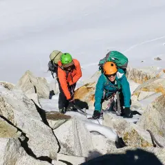 Dos escaladores con mochilas y cascos navegan por rocas y nieve en la montaña. Sus aventuras son como libros abiertos de la naturaleza.
