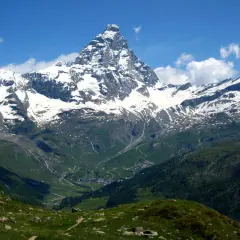 Majestuoso pico nevado se alza sobre un valle verde con un pueblo. El camino de senderismo gr5 etapes serpentea entre las colinas.