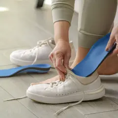 Manos insertando una plantilla azul en una bota blanca. Otra plantilla y una bota están en el suelo.