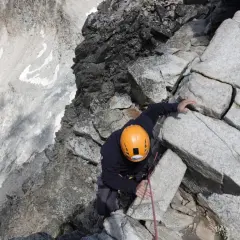 Alpinista con casco naranja escala roca, buscando el aneto por coronas.