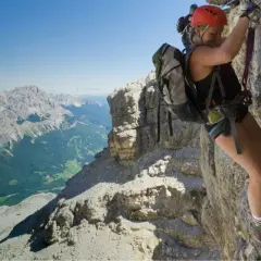 Mujer escalando una vía ferrata en Catalunya, con un paisaje montañoso espectacular de fondo.