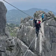 Grupo de personas superando diferentes niveles de vía ferrata, asegurados a cables de acero sobre rocas escarpadas.