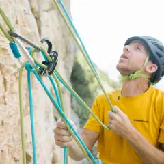 Escalador con casco y camiseta amarilla, asegurando cuerdas de escalada. La **cesta escalada** está lista para la aventura.