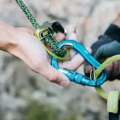 Manos ajustando cuerda y mosquetones azules, esenciales para escalada. Los mejores mosquetones garantizan seguridad.