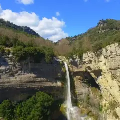 Cascada impresionante en un cañón rocoso, ideal para senderismo en Cataluña. El agua cae en una cortina blanca sobre la piedra dorada.
