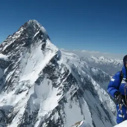 Mikel Zabalza, alpinista, posa con equipo de escalada en la cima de una montaña nevada, con el K2 al fondo.