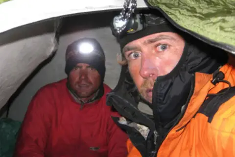 Oscar Pérez, alpinista, y su compañero en una tienda de campaña, ambos con linternas frontales encendidas.