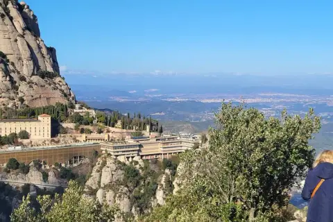 Vista panorámica del monasterio de Sant Miquel de Montserrat, con sus edificios anclados a la montaña y el valle extendiéndose hasta el horizonte.