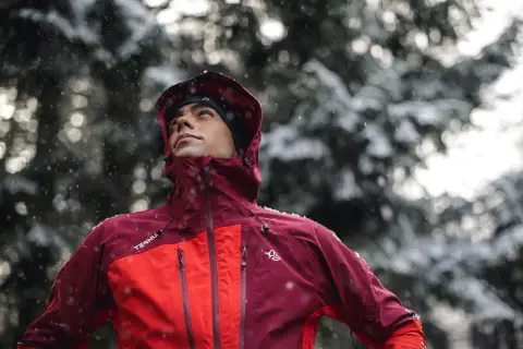 Hombre con ropa para ir a la montaña, con capucha y chaqueta impermeable, bajo una nevada.