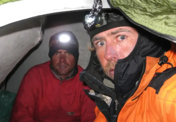 Oscar Pérez, alpinista, y su compañero en una tienda de campaña, ambos con linternas frontales encendidas.