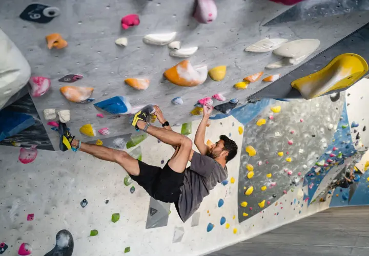 Hombre escalando en un rocódromo interior, superando diferentes grados escalada boulder con agarres de colores.