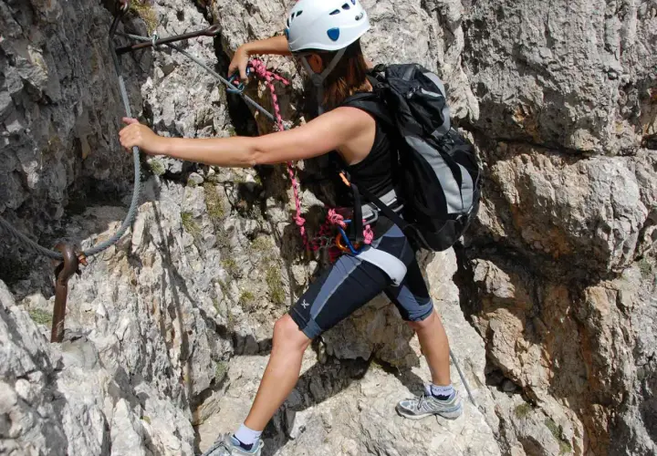 Escaladora en vía ferrata, asegurada con un mosquetón tipo A a un cable de acero en la roca.