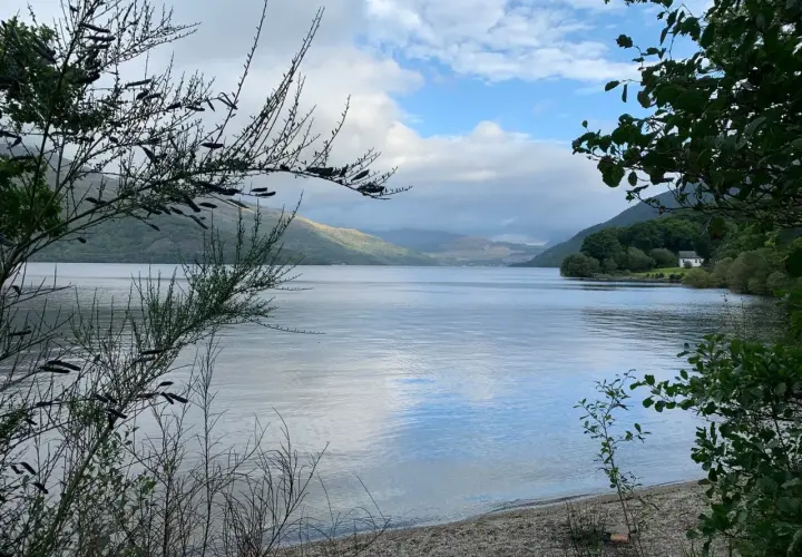Un lago sereno en el West Highland Way, con colinas cubiertas de vegetación y un cielo nublado.
