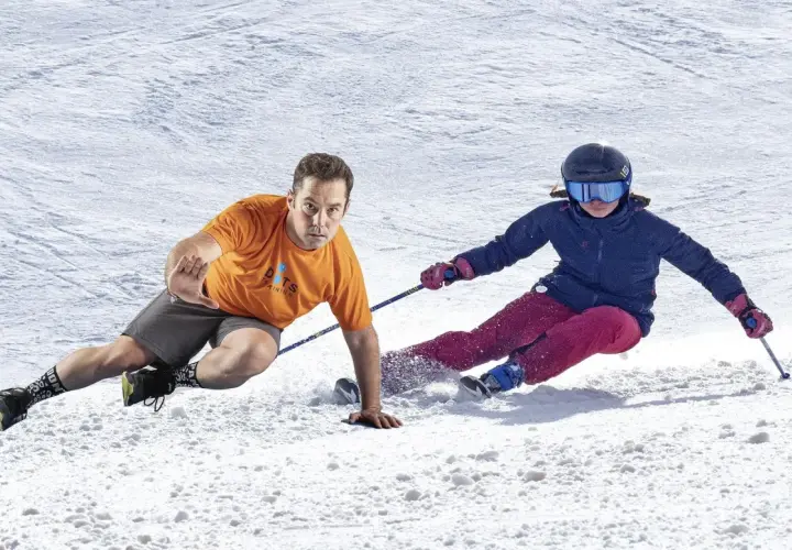 Instructor demuestra ejercicios para esquiar, con un esquiador en la nieve.