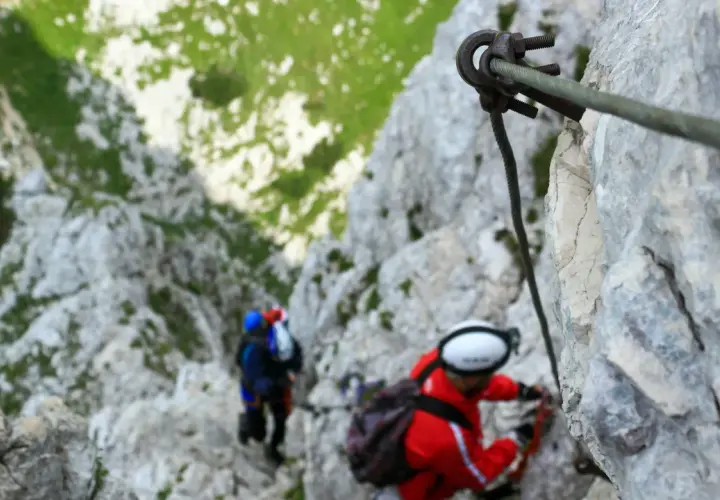 Dos personas en una vía ferrata de iniciación, aseguradas a un cable de acero mientras ascienden por una pared rocosa.