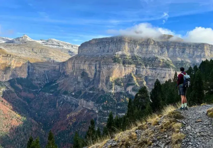 Senderista admira imponentes acantilados y cascadas en las rutas Pirineos. El otoño tiñe el valle de colores cálidos.