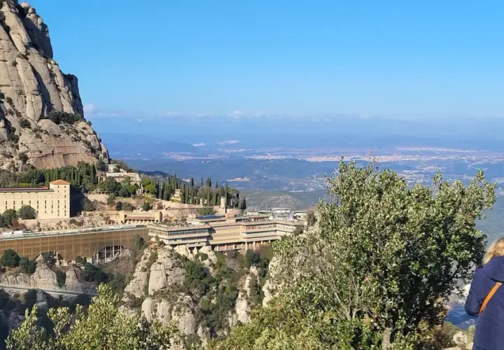 Vista panorámica del monasterio de Sant Miquel de Montserrat, con sus edificios anclados a la montaña y el valle extendiéndose hasta el horizonte.